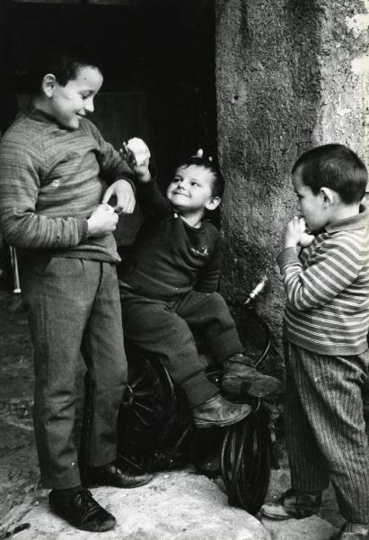 Scena del film "E venne un uomo" - Regia Ermanno Olmi, 1965 - Tre piccoli attori non identificati giocano tra di loro con dei pezzi di pane tra mani. Il bambino in centro è seduto sulla canna dell'acqua mentre quello a destra mangia un pezzo di pane.