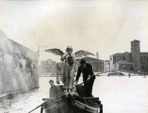 Scena del film "E venne un uomo" - Regia Ermanno Olmi, 1965 - Su una gondola, attraversando i canali veneziani, due attori non identificati portano una statua di un angelo con un vaso nelle mani.