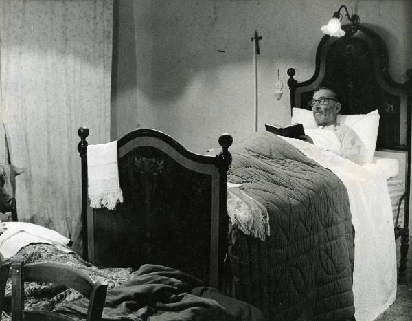 Scena del film "E venne un uomo" - Regia Ermanno Olmi, 1965 - Un attore non identificato è sdraiato in un letto mentre legge un libro.