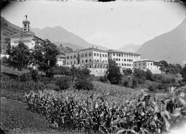 Valnegra. Veduta panoramica con la chiesa parrocchiale di San Michele, il Collegio San Carlo e, in primo piano, un campo di granoturco