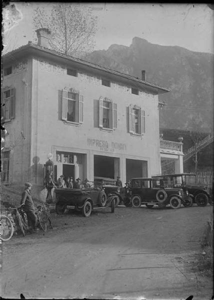 Piazza Brembana. Prima sede dell'impresa di autotrasporti Donati. Automobili, tra cui una Fiat 502, un'Esperia e un'Adler, in sosta davanti e dentro la rimessa. Distributore di benzina Shell