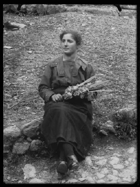 Val Brembana. Ritratto di giovane donna con mazzo di fiori seduta su un muretto in un prato