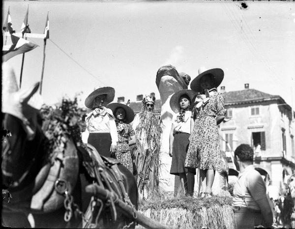 Ritratto di gruppo - Quattro mondine e un uomo in costume su di carro allegorico con rana gigante trainato da un cavallo - Garlasco - Festa delle mondine - Bandiere italiane