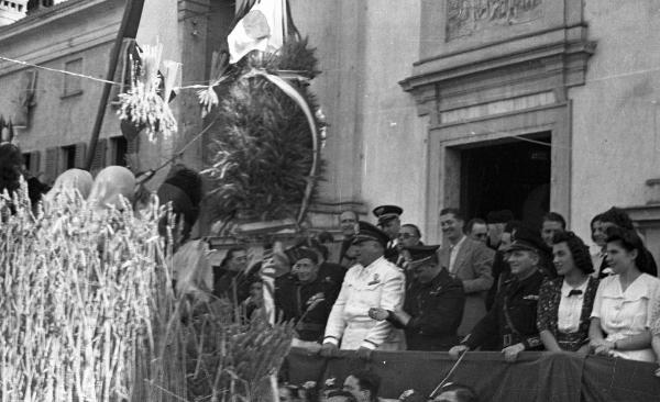 Garlasco - Piazza della Repubblica (già Vittorio Emanuele II) - Festa delle mondine - Palco delle autorità con esponenti del Partito Fascista - Bandiera italiana - Carro allegorico - Chiesa della Beata Assunta, scorcio