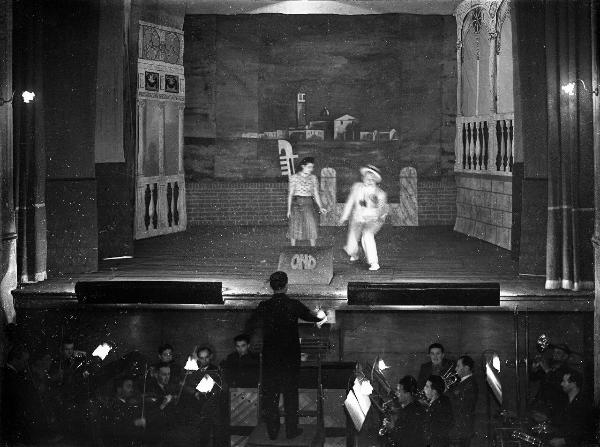 Garlasco - Via Santissima Trinità 6 - Teatro Martinetti - Interno - Palcoscenico con due persone - Quinte sceniche e fondale - Buca d'orchestra e maestro in posizione centrale e sopraelevata - Scritta O.N.D. sulla copertura della buca del suggeritore