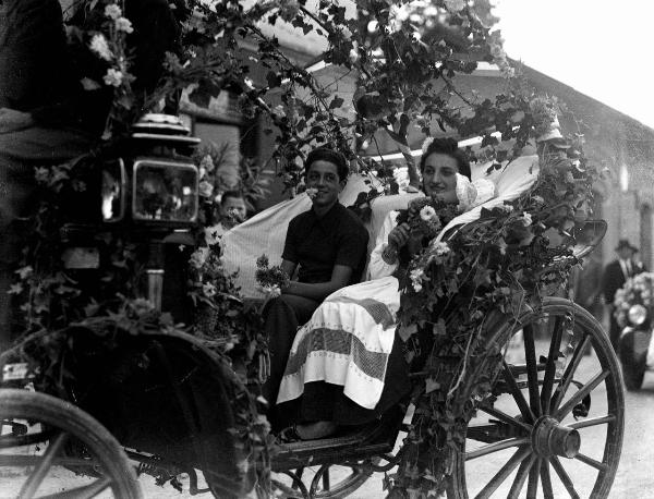Ritratto di gruppo - Una giovane donna in abiti tradizionali e un ragazzo seduti sulla carrozza addobbata di fiori, tralci e grappoli d'uva - Salice Terme - Festa dell'uva