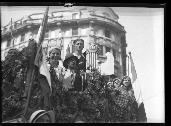 Pavia - Piazza Castello - 3° Festa nazionale dell'uva - Carro decorato con tralci di vite e grappoli d'uva e gruppo di persone in abiti tradizionali con fascio littorio e bandiera italiana - Palazzo Devoti sullo sfondo