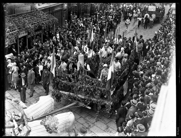 Pavia - Corso Strada Nuova - 3° Festa nazionale dell'uva - Sfilata dei carri allegorici decorati con tralci di vite e grappoli d'uva - Folla di persone distribuia ai lati della strada - Negozio adornato con grappoli d'uva e tralci di vite