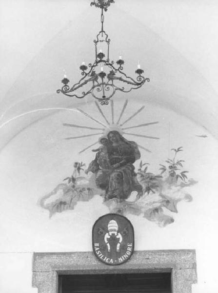 Madonna del Bosco. Lunetta sovrapporta con affresco raffigurante Madonna con Bambino. Sopra la porta insegna con scritta: "Basilica minore". Lampadario in ferro battuto all'incrocio della crociera.