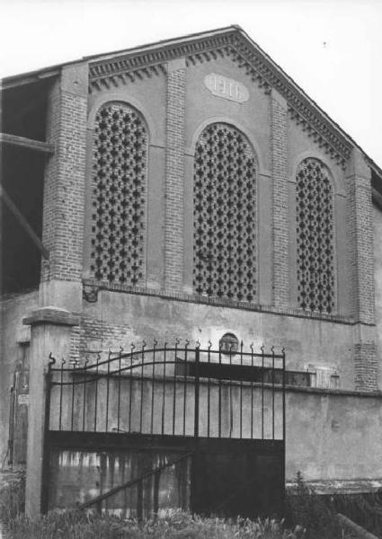 Muro esterno di fienile con tre grandi fornici chiusi con mattoni a nido d'ape. Al centro scritta: "1916".