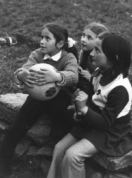 Tre bambine sedute in un prato rispondono alle domande dell'intervistatore.