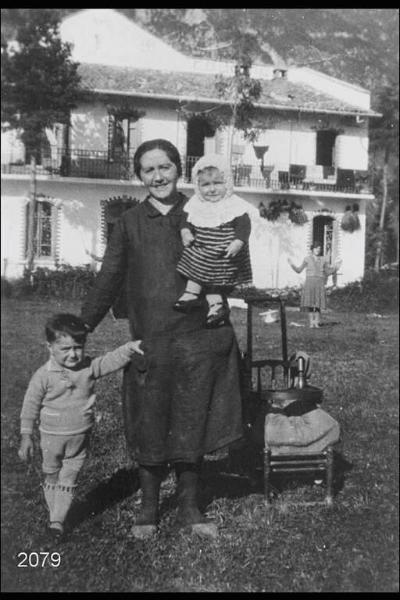 Eva Angiolini con due figli. Esterno. Prato davanti a edificio rurale.