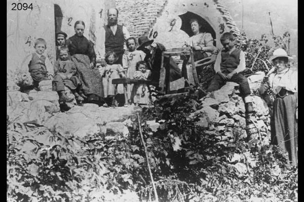 Famiglia Giovanni Vitari. Gruppo in posa liberamente disposto sul muretto davanti a una casa di montagna.