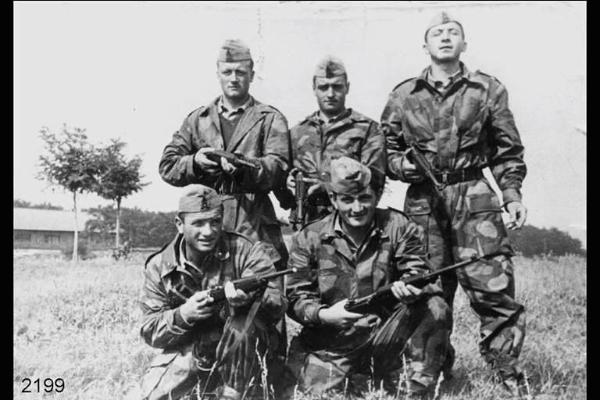 Gruppo di soldati di leva: il 1° in piedi Germano Salvi. Cinque ragazzi armati in posa con tute mimetiche, in un campo.