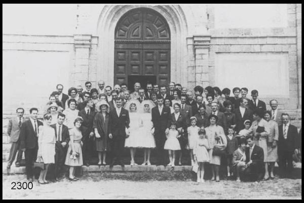 Nozze delle sorelle Maria e Letizia Manzinali. Posa di gruppo a figura intera in esterno, sul sagrato della chiesa. Le due coppie sono in abito per cerimonia.