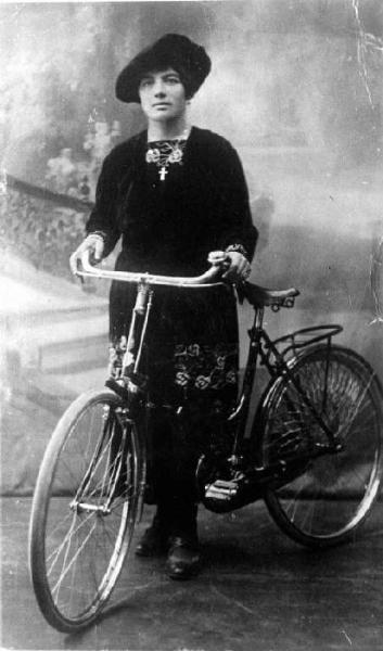 Maddalena Invernizzi. Posa frontale in studio a figura intera, con bicicletta.