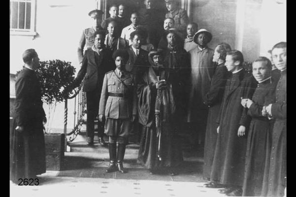 Autorità laiche ed ecclesiastiche d'Etiopia in visita in Italia. Posa all'esterno di edificio. Militare etiope e personaggio in costume in primo piano.