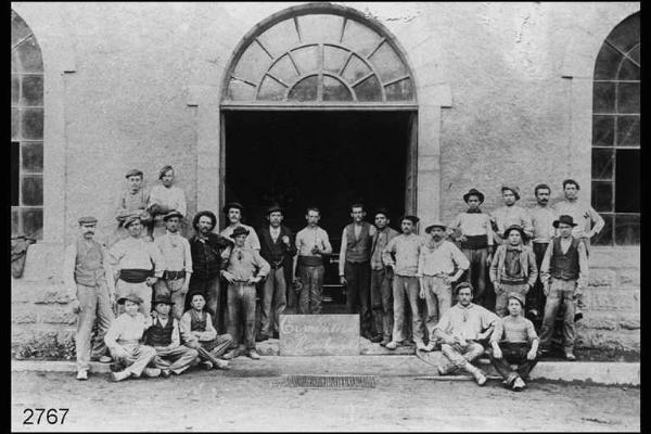 Cementerie Rumelange. Maestranze provenienti da Rota d'Imagna in posano all'ingresso della fabbrica. Davanti a loro, lastra di pietra con la scritta: "Cementerie Romelange".