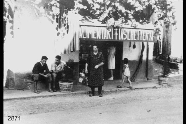 Virginia Pelaratti e i nipoti all'esterno di un negozio. Sulla tenda la scritta: "ALIMENTARI FIASCHETTERIA".
