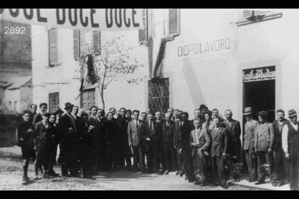 Inaugurazione della sede del Dopolavoro. Sull'edificio, la scritta: "DOPOLAVORO". In piazza, lo striscione: "DUCE DUCE DUCE".