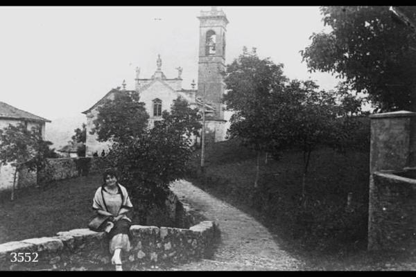 Chiesa di Rotadentro. In primo piano di signora seduta su un muretto.