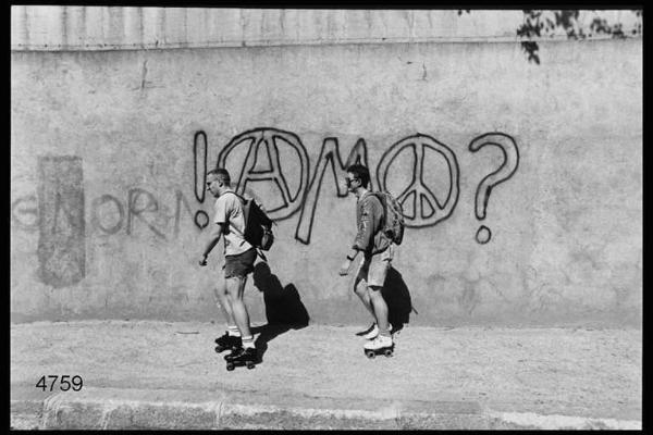 Coppia di giovani pattina. Sul fondo muro con graffiti.