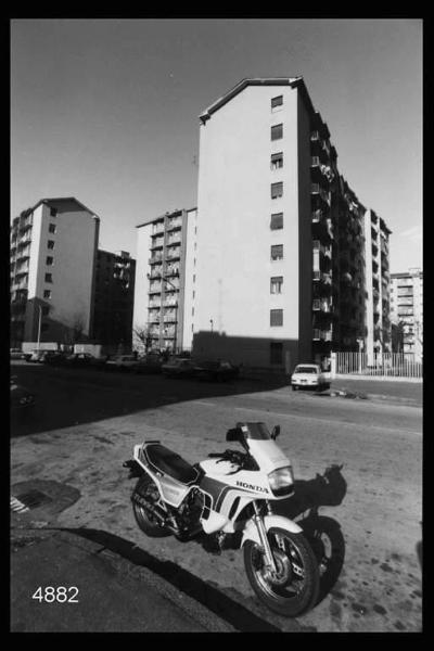 Quarto Oggiaro. Una via del quartiere: in primo piano una moto, sullo sfondo alcuni condominii.