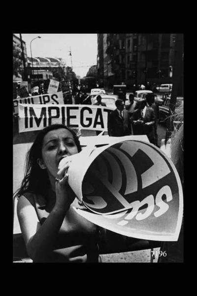 Manifestazione sindacale. In primo piano donna che urla in un manifesto arrotolato a forma di cono per amplificare la voce. ullo sfondo striscioni di impiegati e di lavoratori Philips. Foto acquisita per la mostra < Dai campi dalle officine >.