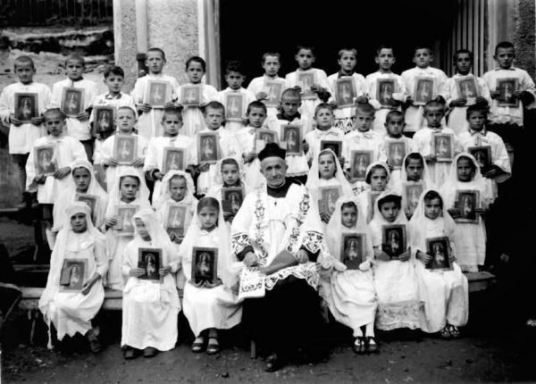 Sacerdote e gruppo di bambini con immagini sacre.