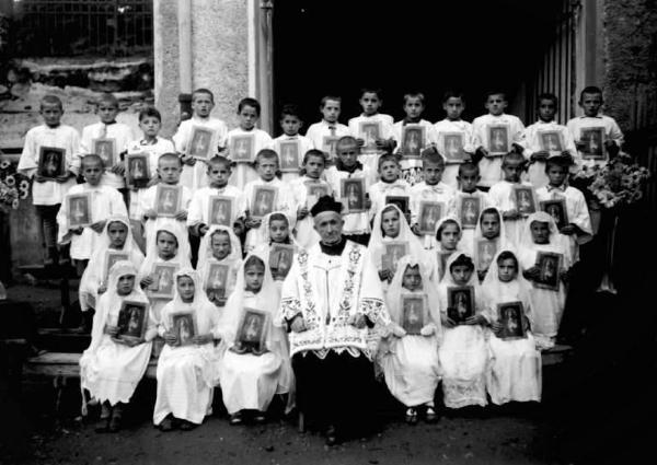 Sacerdote e gruppo di bambini con immagini sacre.