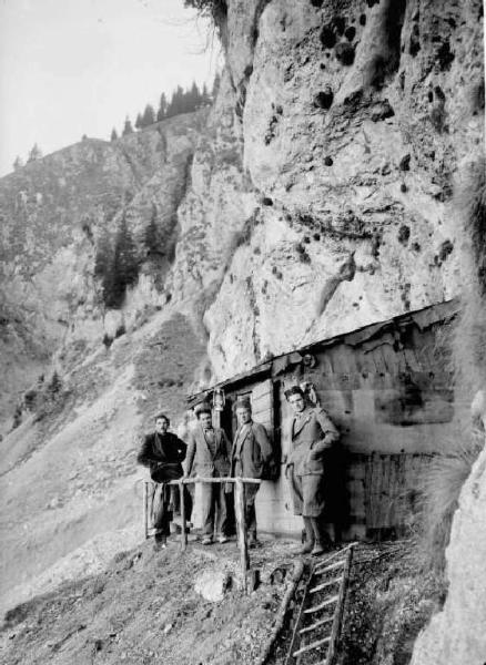 Quattro uomini davanti ad una baracca sotto una parete rocciosa