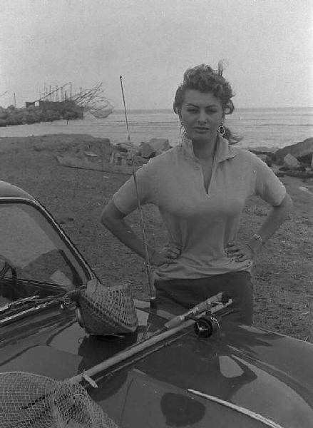 Località non identificata. Sofia Loren, vicino ad un'automobile, sulla spiaggia