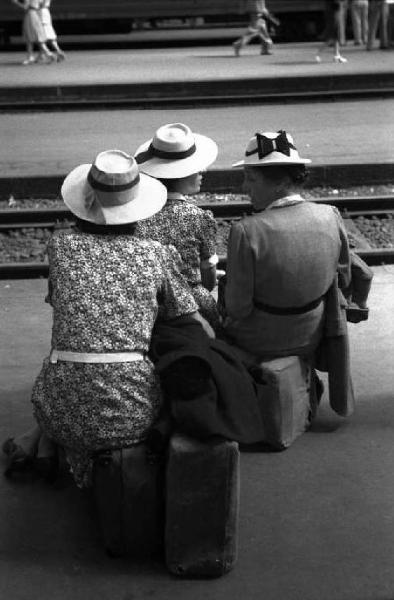Milano. Stazione Centrale. Viaggiatrici in attesa, sedute sui bagagli, vicino ai binari