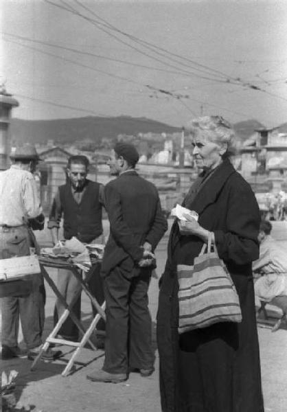 Genova. Ritratto di donna anziana. Sullo sfondo persone al mercato