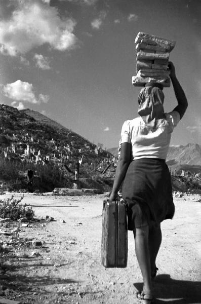 Nuova Cassino - Ricostruzione - Ritratto femminile: donna profuga di spalle con valigia