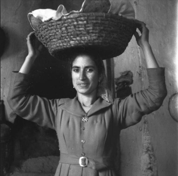 Melissa (Crotone) - Giovane donna con una cesta di pane sulla testa nella cucina di una casa
