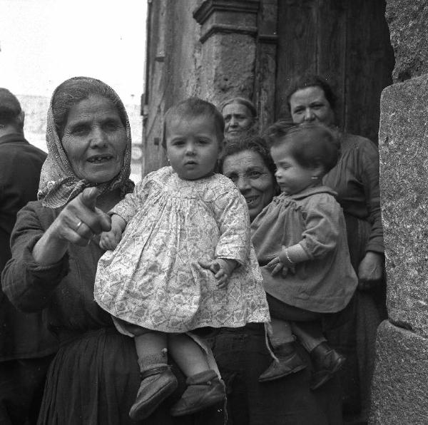 Melissa (Crotone) - Due donne con bambini in braccio e altre donne sul portone di un edificio