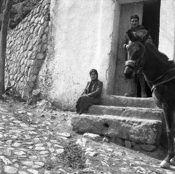 Melissa (Crotone) - Uomo sull'uscio, donna seduta su gradini e mulo all'esterno di una casa