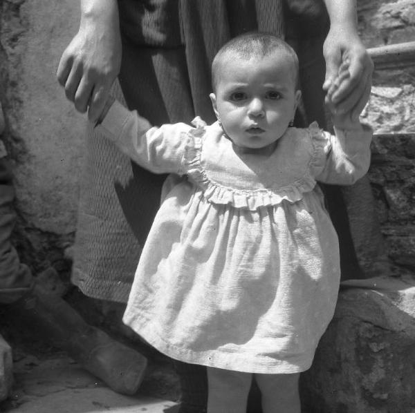 Melissa (Crotone) - Donna con bambino ai primi passi all'esterno di una casa