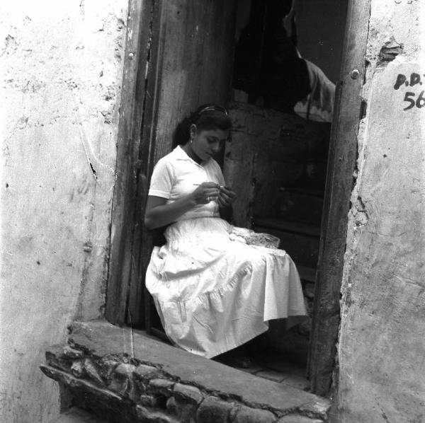 Melissa (Crotone) - Giovane donna che ricama sull'uscio di una casa