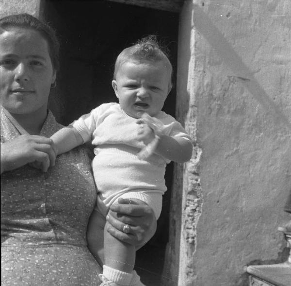 Melissa (Crotone) - Donna con bambino in braccio all'esterno di una casa