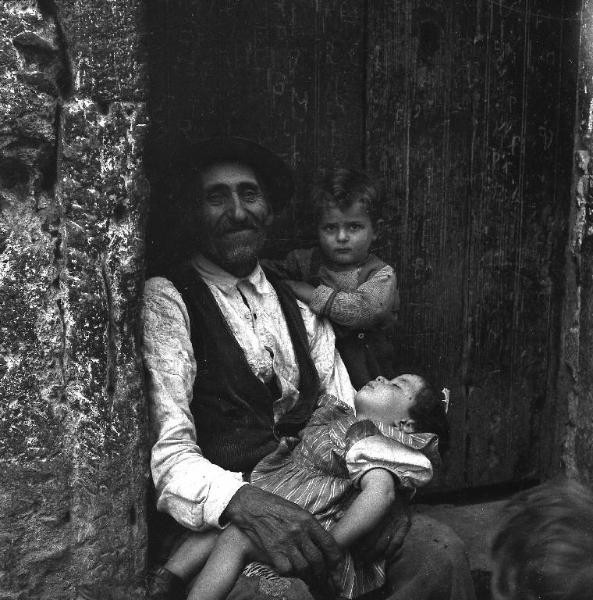 Melissa (Crotone) - Uomo anziano con bambina in braccio e altro bambino seduto sul gradino di entrata di una casa
