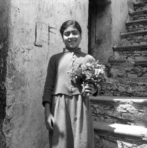 Melissa (Crotone) - Ragazza con mazzolino di fiori all'esterno di una casa - Ritratto