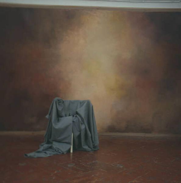 Still-life: sedia ricoperta da un drappo si staglia su fondale nello studio del fotografo