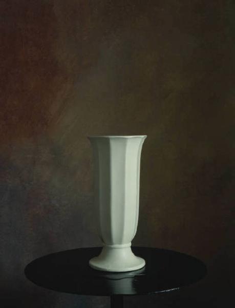 Still-life: vaso in porcellana bianca, appoggiato su un tavolino nero, si staglia su fondale nello studio del fotografo