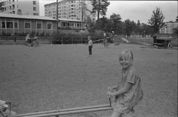 Svezia - Bambina sull'altalena e altri bambini che giocano - Sullo sfondo palazzi cittadini