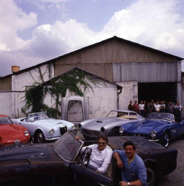 Autofficina macchine sportive - i titolari  posano di fianco a una vettura all'esterno dell'officina