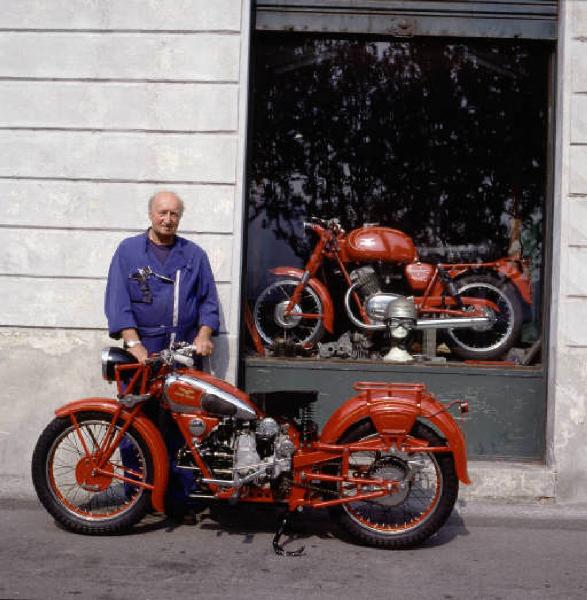 Officina di moto d'epoca - il titolare posa accanto a una motocicletta davanti alla vetrina del motosalone