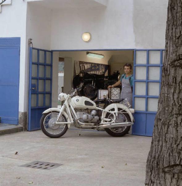 Officina di moto d'epoca - il titolare in posa accanto a una motocicletta sull'ingresso dell'officina