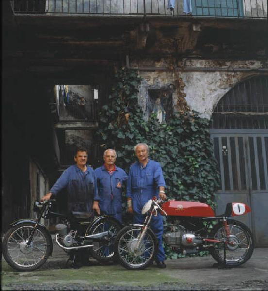 Officina di moto d'epoca - meccanici in posa accanto a una motocicletta nel cortile